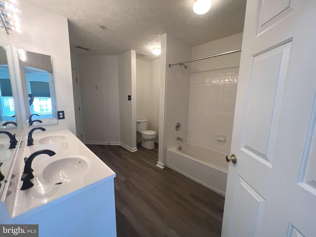 full bathroom featuring wood finished floors, a textured ceiling, toilet, double vanity, and shower / bathtub combination