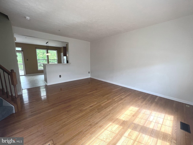 unfurnished room with wood finished floors, stairway, baseboards, a textured ceiling, and a smoke detector