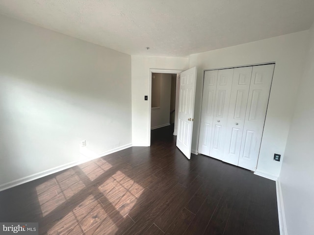 unfurnished bedroom featuring dark wood-type flooring, baseboards, and a closet