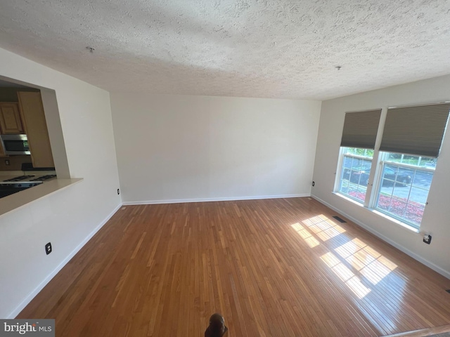 unfurnished living room featuring wood finished floors, a textured ceiling, and baseboards