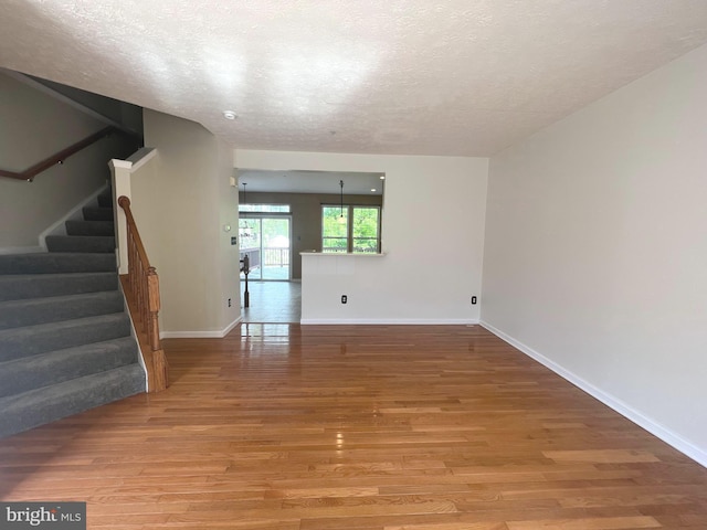 unfurnished room featuring light wood-style flooring, a textured ceiling, stairway, and baseboards