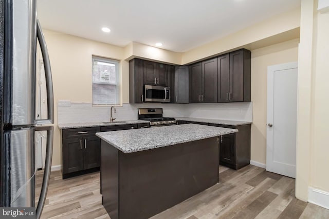 kitchen featuring stainless steel appliances, a sink, dark brown cabinets, light wood finished floors, and light stone countertops