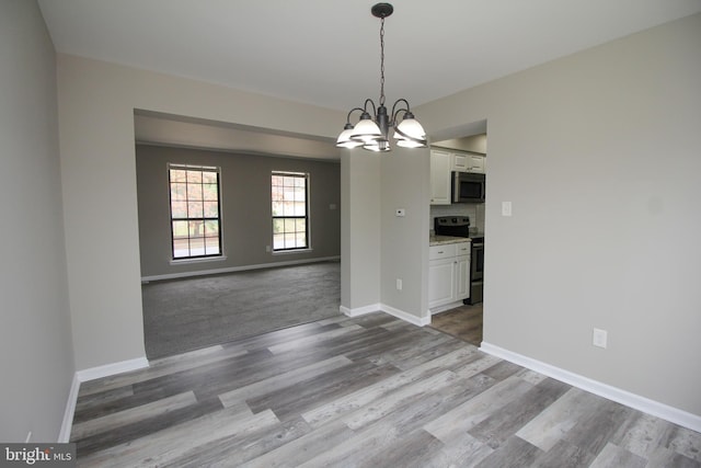 unfurnished dining area with wood finished floors, baseboards, and a chandelier