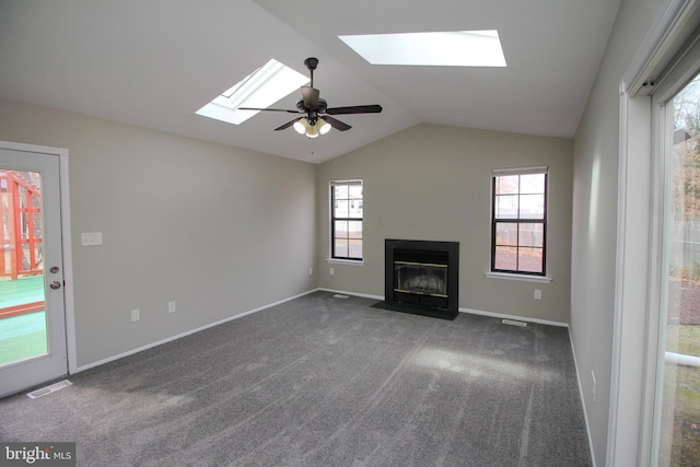 unfurnished living room featuring a skylight, vaulted ceiling, a fireplace with flush hearth, a ceiling fan, and dark carpet
