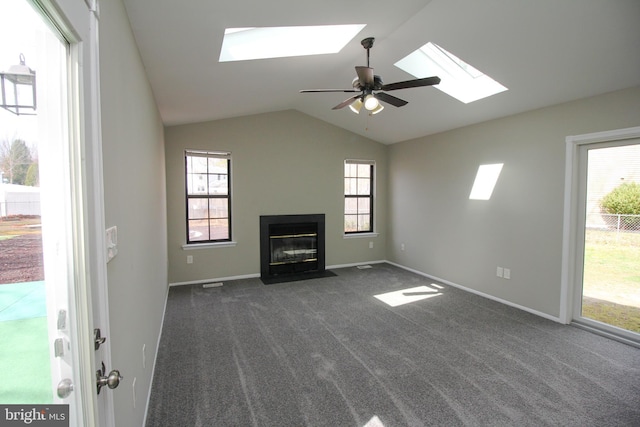 unfurnished living room featuring a skylight, vaulted ceiling, dark colored carpet, ceiling fan, and a fireplace with flush hearth