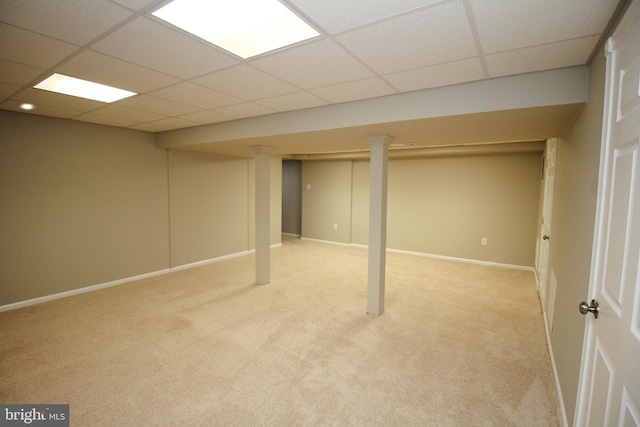 finished basement featuring a paneled ceiling, light colored carpet, and baseboards
