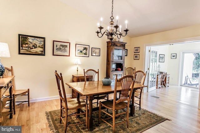 dining space featuring a chandelier, light wood-style floors, lofted ceiling, and baseboards