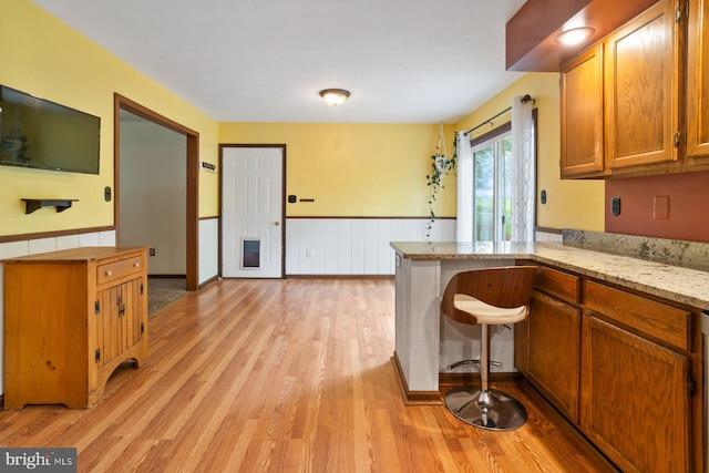 101 George St, Taneytown, MD 21787 - kitchen featuring light wood-style floors, a wainscoted wall, brown cabinetry, a peninsula, and light stone counters