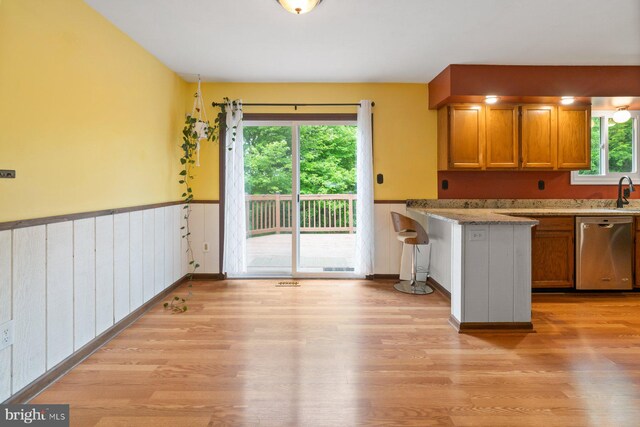 101 George St, Taneytown, MD 21787 - kitchen with stainless steel dishwasher, brown cabinets, light wood-type flooring, a wainscoted wall, and a peninsula