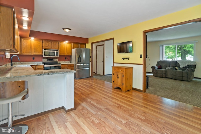 101 George St, Taneytown, MD 21787 - kitchen with stainless steel appliances, a sink, light wood-style floors, a peninsula, and brown cabinetry