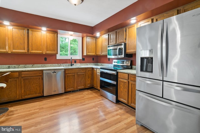 101 George St, Taneytown, MD 21787 - kitchen featuring stainless steel appliances, a sink, brown cabinets, light wood-type flooring, and light stone countertops