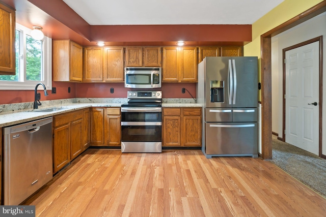 101 George St, Taneytown, MD 21787 - kitchen featuring stainless steel appliances, a sink, light wood-type flooring, brown cabinetry, and light stone counters