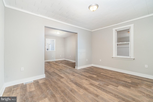 empty room featuring ornamental molding, wood finished floors, and baseboards