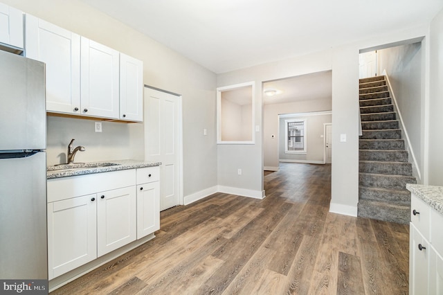 kitchen with freestanding refrigerator, a sink, wood finished floors, white cabinets, and baseboards
