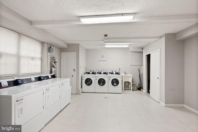 communal laundry room with washer and clothes dryer, a textured ceiling, and baseboards
