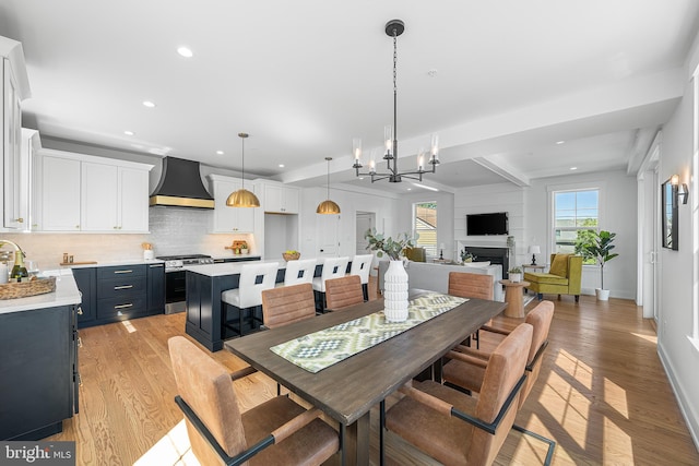 dining room featuring light wood-style flooring, recessed lighting, a chandelier, baseboards, and a fireplace