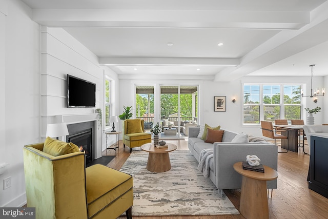 living area with beam ceiling, wood finished floors, a glass covered fireplace, recessed lighting, and a chandelier
