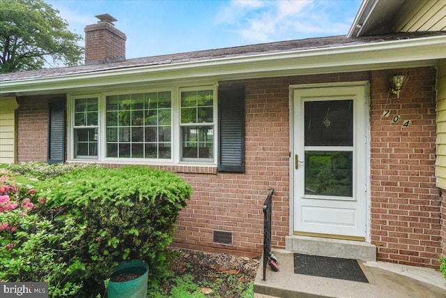 view of exterior entry featuring brick siding and a chimney