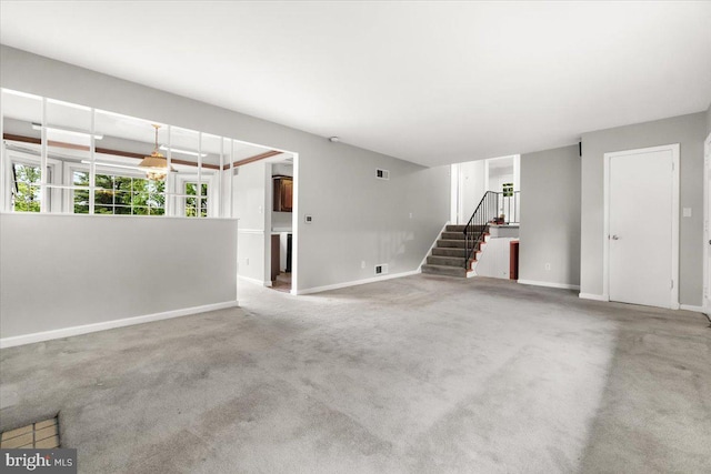 unfurnished living room featuring baseboards, stairway, and carpet floors