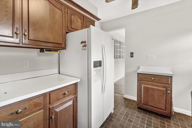 kitchen with white refrigerator with ice dispenser, light countertops, brown cabinets, and baseboards