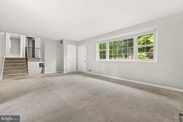 unfurnished living room featuring baseboards, carpet floors, and stairway