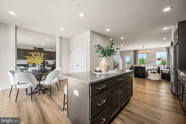 kitchen featuring freestanding refrigerator, light wood-style floors, a center island, recessed lighting, and a kitchen bar
