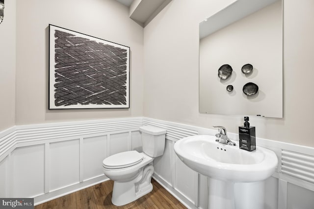half bath featuring a wainscoted wall, wood finished floors, toilet, a decorative wall, and a sink