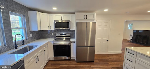 kitchen with stainless steel appliances, a sink, light stone counters, dark wood finished floors, and white cabinets