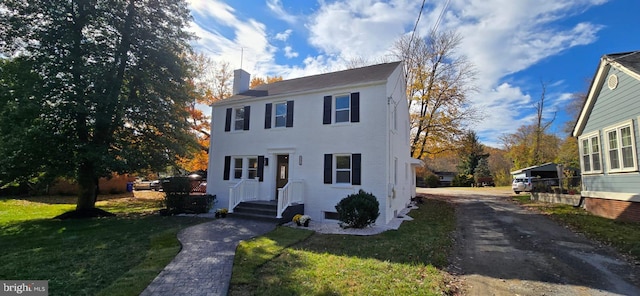 colonial home featuring a chimney, a front lawn, and brick siding