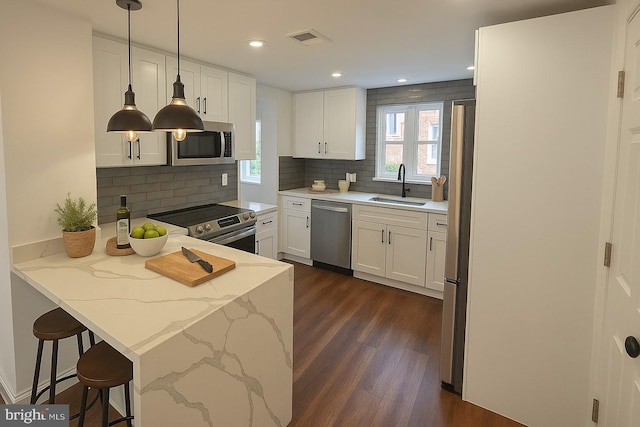 kitchen featuring stainless steel appliances, a sink, a peninsula, dark wood-style flooring, and white cabinetry