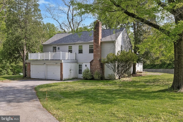 view of front facade with driveway, a chimney, a balcony, a front lawn, and a garage