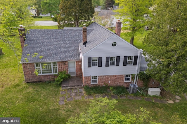 view of front of house with a chimney, a front yard, brick siding, and cooling unit