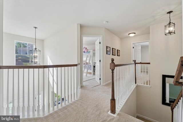 hallway featuring an upstairs landing, a chandelier, carpet, and baseboards