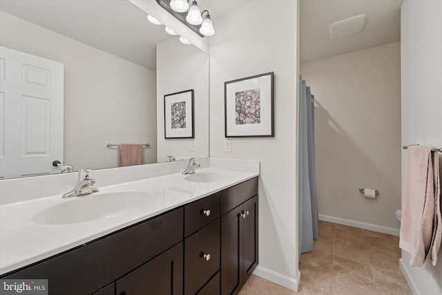 bathroom with toilet, double vanity, baseboards, and tile patterned floors
