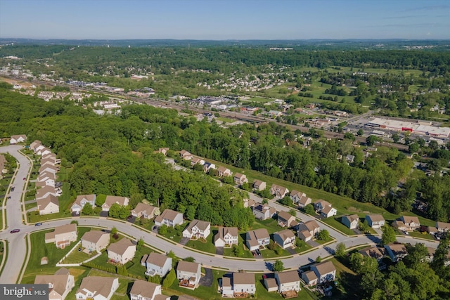 aerial view of property and surrounding area featuring nearby suburban area and a heavily wooded area