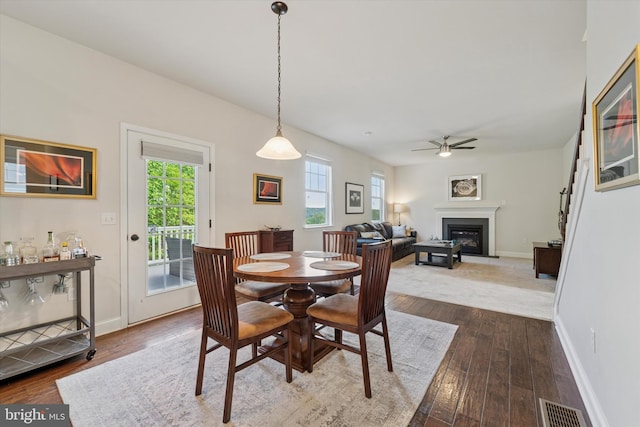 dining space featuring a glass covered fireplace, dark wood-type flooring, ceiling fan, and baseboards