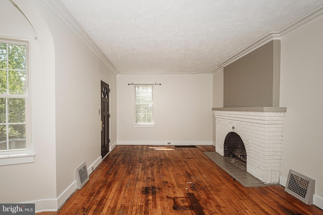 unfurnished living room featuring a brick fireplace, hardwood / wood-style floors, a textured ceiling, baseboards, and crown molding