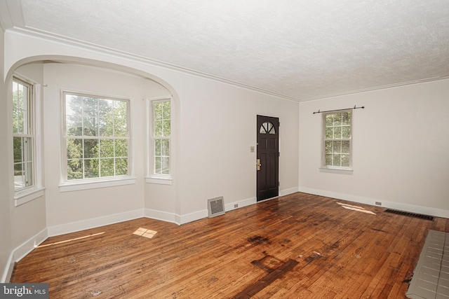 empty room featuring a textured ceiling, wood-type flooring, crown molding, healthy amount of natural light, and baseboards