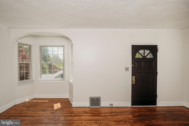 entryway with a textured ceiling, wood finished floors, ornamental molding, baseboards, and arched walkways