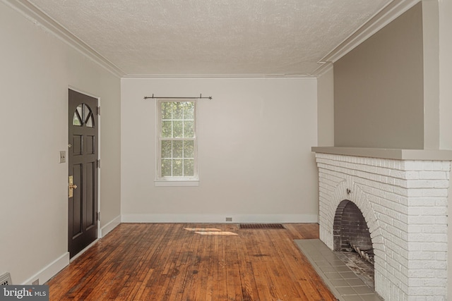 unfurnished living room with hardwood / wood-style floors, crown molding, a textured ceiling, a brick fireplace, and baseboards