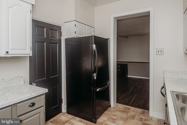 kitchen featuring freestanding refrigerator, white cabinetry, and light stone finish floors
