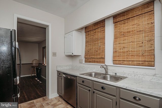 kitchen featuring freestanding refrigerator, dishwasher, gray cabinets, a sink, and light countertops
