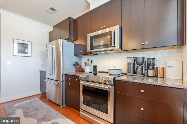 kitchen with appliances with stainless steel finishes, light wood-type flooring, tasteful backsplash, and light stone countertops