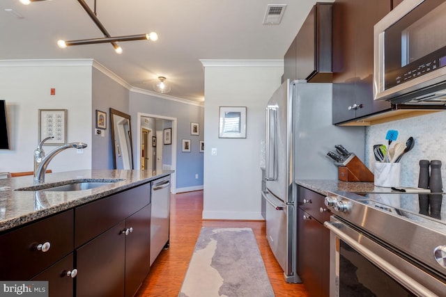 kitchen featuring stainless steel appliances, a sink, crown molding, light wood-style floors, and stone countertops