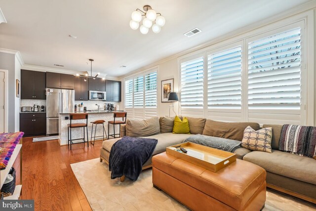 living room featuring light wood-style floors, ornamental molding, and a chandelier