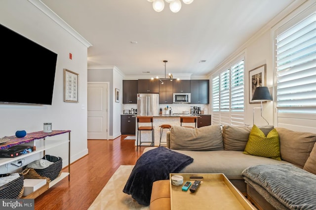 living area featuring crown molding, light wood-style floors, a chandelier, and baseboards
