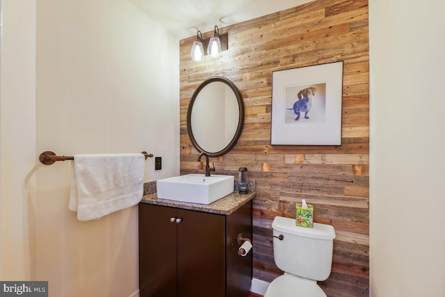 half bathroom with wooden walls, vanity, and toilet