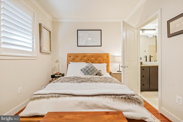 bedroom with ensuite bathroom, crown molding, a sink, wood finished floors, and baseboards