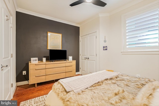 bedroom with wood finished floors, ornamental molding, baseboards, a closet, and ceiling fan