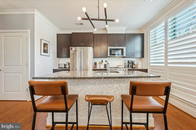 kitchen featuring stainless steel appliances, a kitchen breakfast bar, ornamental molding, light wood-style flooring, and tasteful backsplash